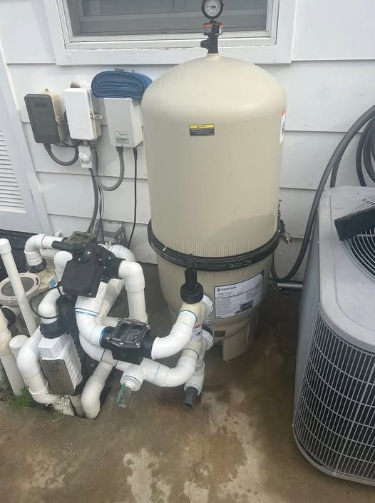 A swimming pool filter is sitting on the ground next to an air conditioner.