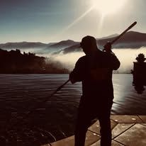 A man is standing on a dock holding a stick in front of a lake.