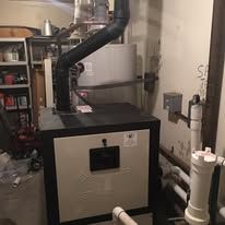A boiler is sitting in a basement next to a water heater.