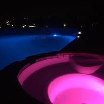 A swimming pool is lit up at night with pink lights.