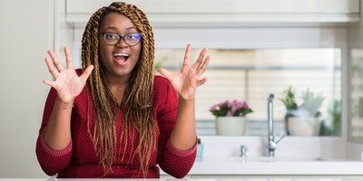 A woman is sitting at a table in a kitchen with her hands in the air.