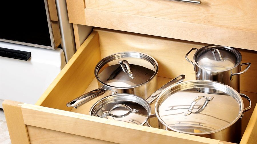 A wooden drawer filled with stainless steel pots and pans