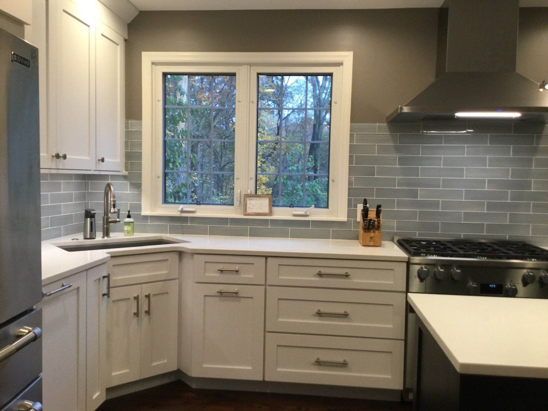A kitchen with white cabinets , a stove , a sink and a window.