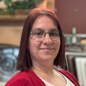 A woman wearing glasses and a red sweater is smiling for the camera.