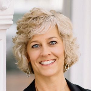 A woman with blonde hair and blue eyes is smiling for the camera.