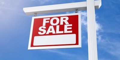A red and white for sale sign against a blue sky