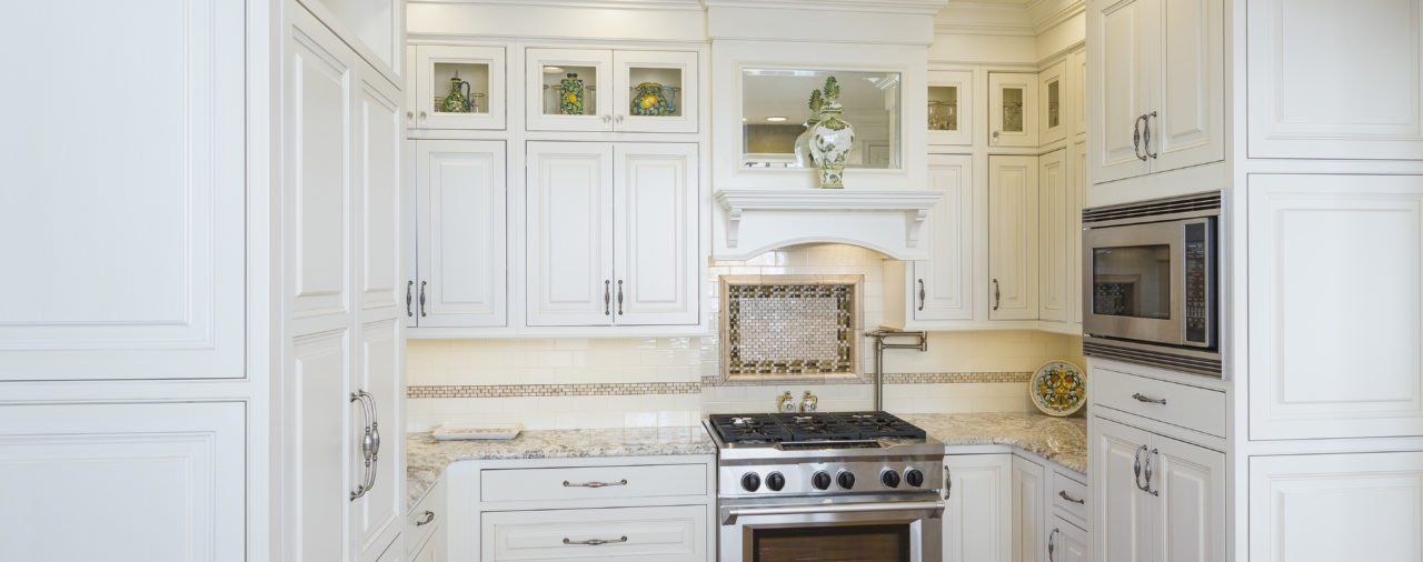 A kitchen with white cabinets , a stove , a microwave , and a sink.