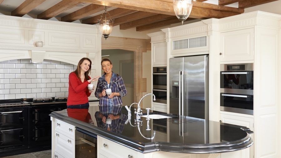 A man and a woman are standing in a kitchen drinking coffee.