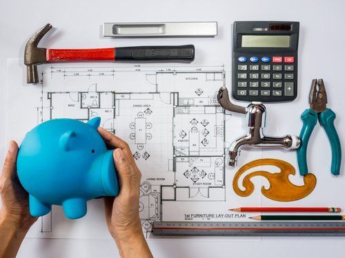 A person is holding a blue piggy bank in front of a blueprint.
