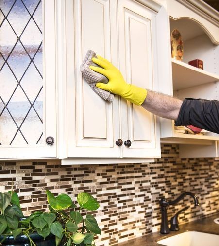 A person wearing yellow gloves is cleaning a cabinet in a kitchen