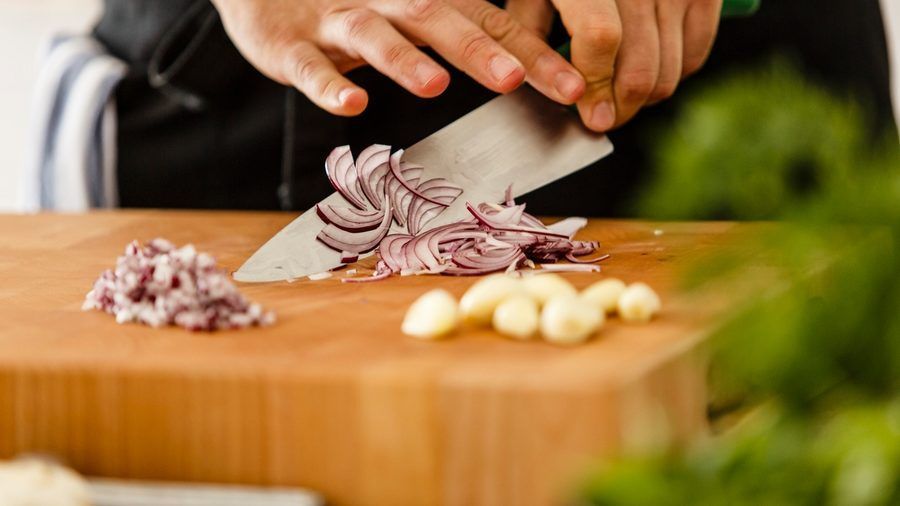 A person is cutting onions and garlic on a cutting board.