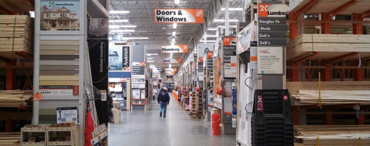 A man is walking down a very long hallway of a hardware store.