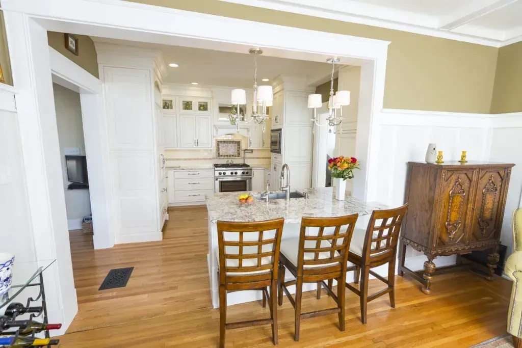 A dining room with a table and chairs and a kitchen in the background.