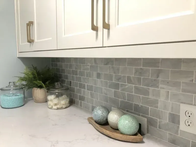 A kitchen counter with white cabinets and a marble tile backsplash.