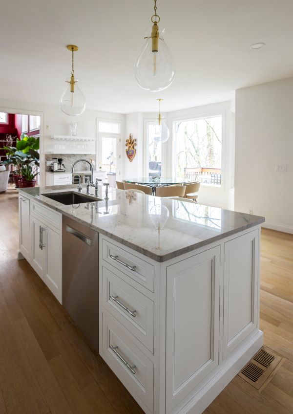 A kitchen with white cabinets , a large island , a sink , and a dishwasher.