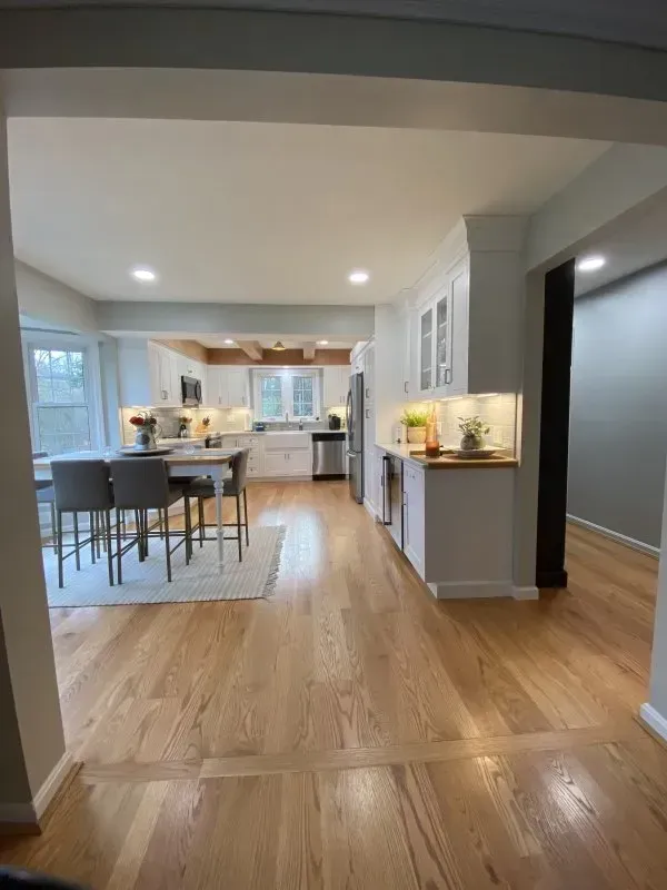 A kitchen and dining room in a house with hardwood floors and white cabinets.