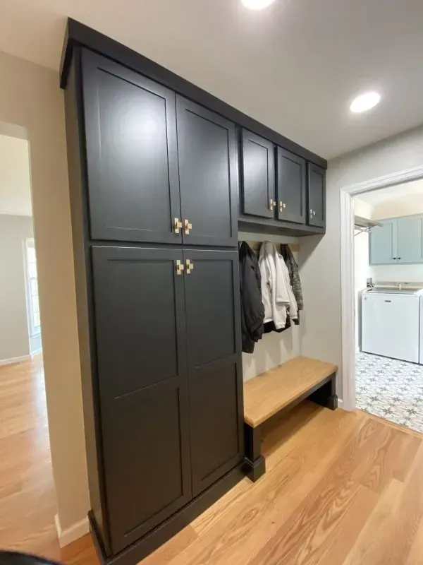 A laundry room with black cabinets and a wooden bench