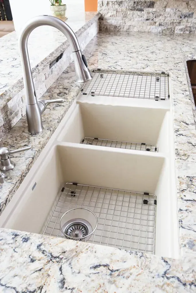 A kitchen sink with two sinks and a faucet on a granite counter top.