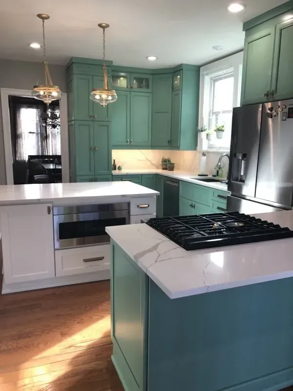 A kitchen with green cabinets , white counter tops , stainless steel appliances and a large island.