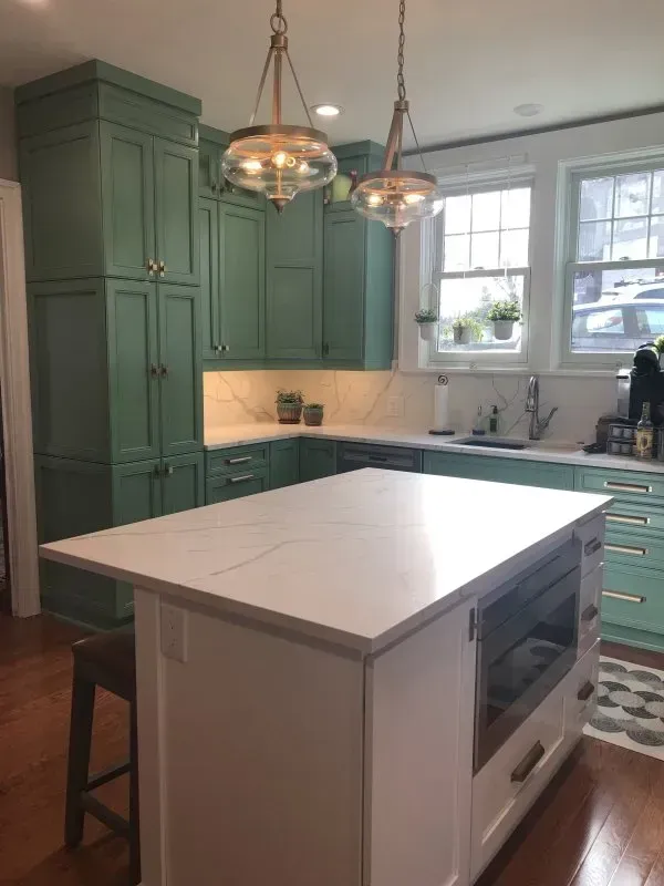 A kitchen with green cabinets and a white island.
