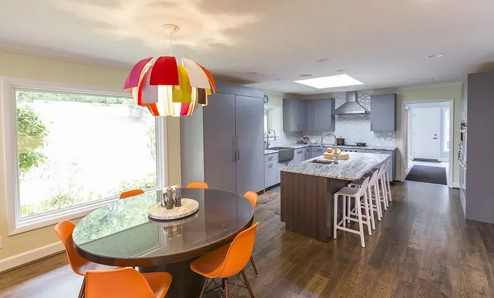 A dining room with a round table and orange chairs in a kitchen.