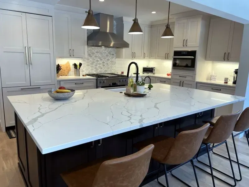 A kitchen with white cabinets and a large island with a marble counter top.