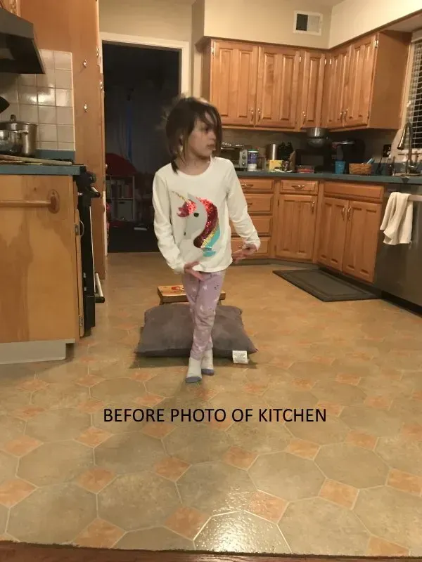 A little girl is standing on a pillow in a kitchen.