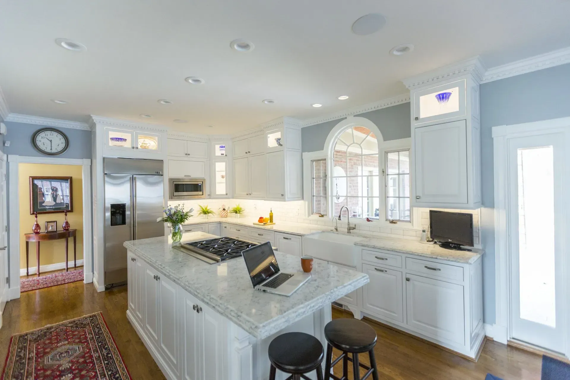 A kitchen with white cabinets and stainless steel appliances and a laptop on the counter.