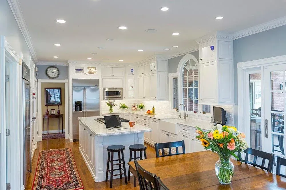 A kitchen with white cabinets , stools , a table and a vase of flowers.