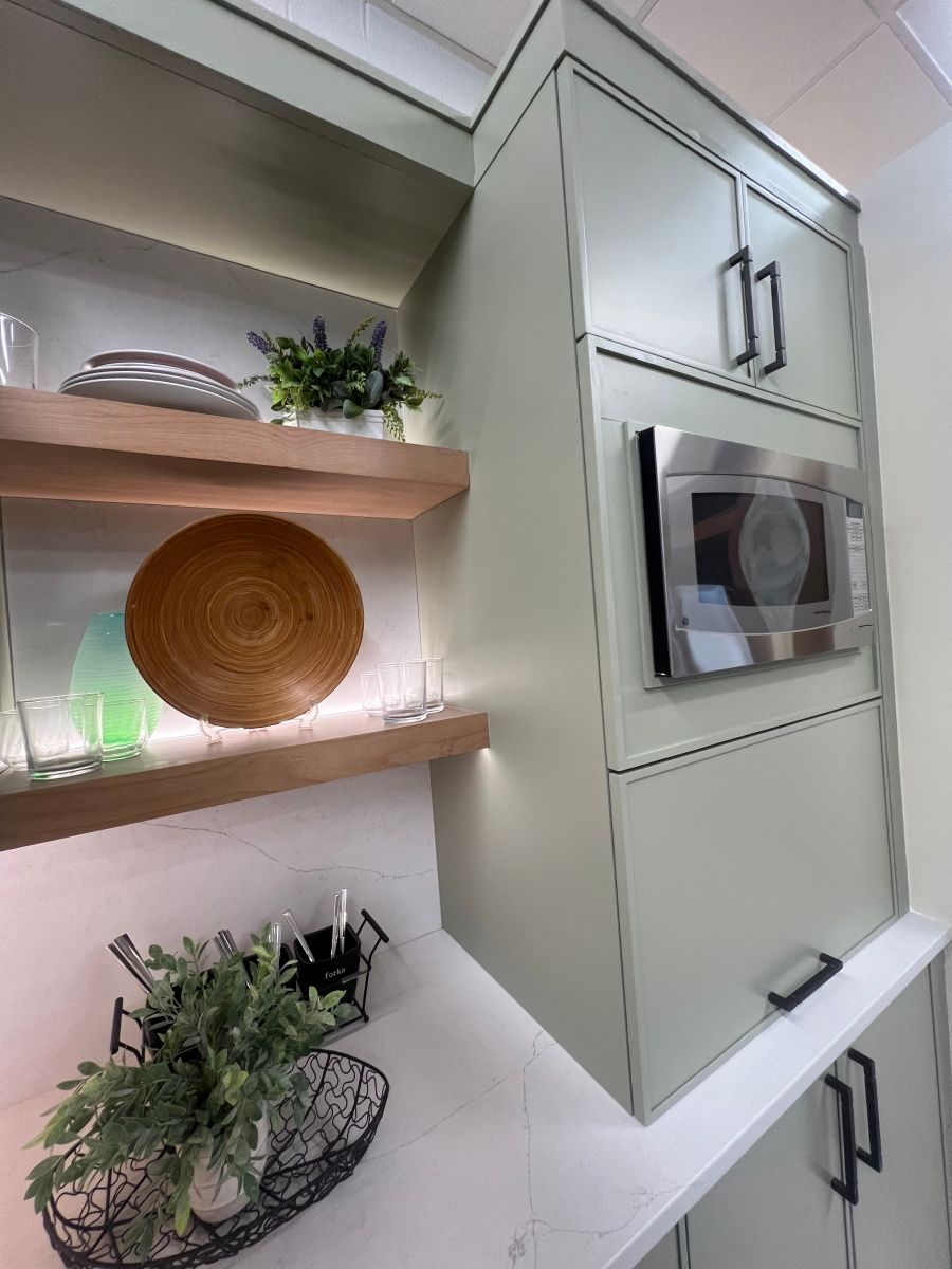 A kitchen with green cabinets and a microwave on the wall.
