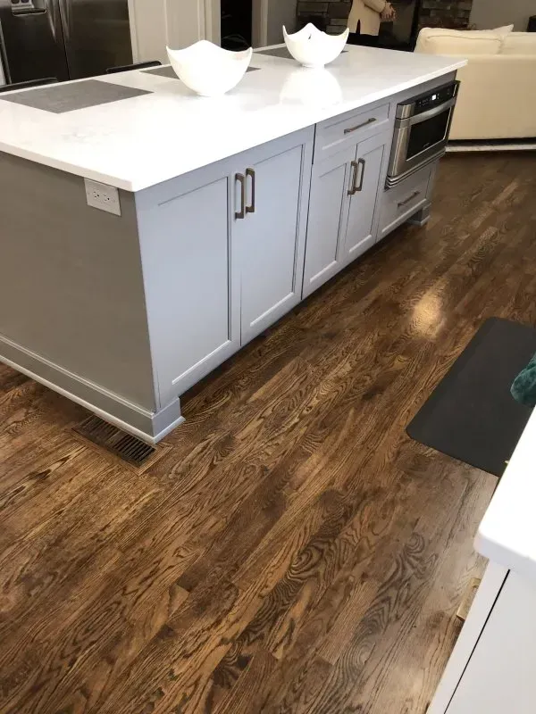 A kitchen with hardwood floors , white cabinets and a large island.