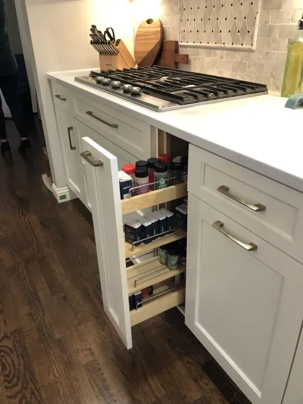 A kitchen with white cabinets and a pull out drawer filled with spices.