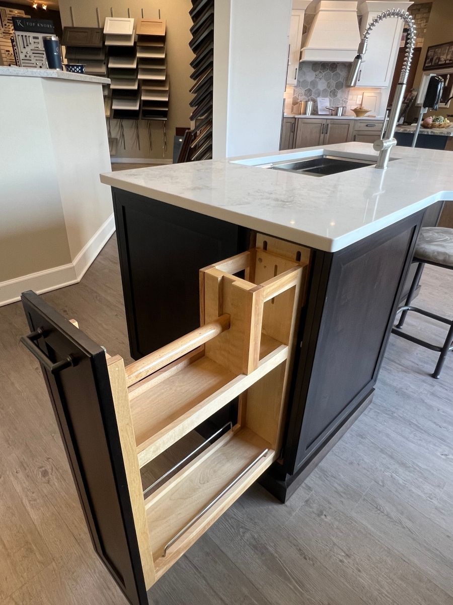 A kitchen island with a pull out spice rack and a sink.