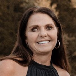 A woman in a black dress and hoop earrings is smiling for the camera.