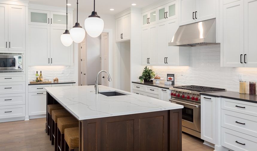 A kitchen with white cabinets , granite counter tops , stainless steel appliances and a large island.