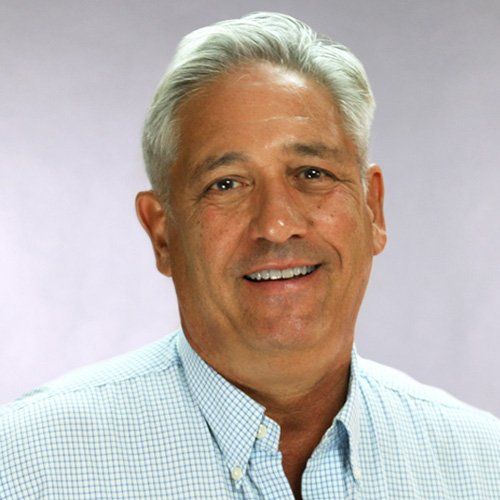 A man with gray hair and a blue shirt is smiling for the camera.