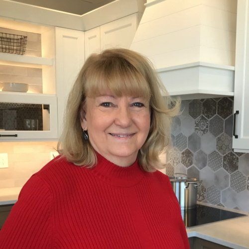 A woman in a red sweater is smiling in a kitchen.