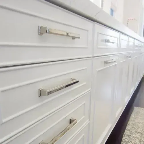 A kitchen with white cabinets and stainless steel drawer handles.