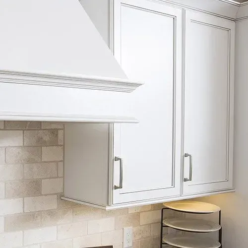A kitchen with white cabinets and a hood above the cabinets.