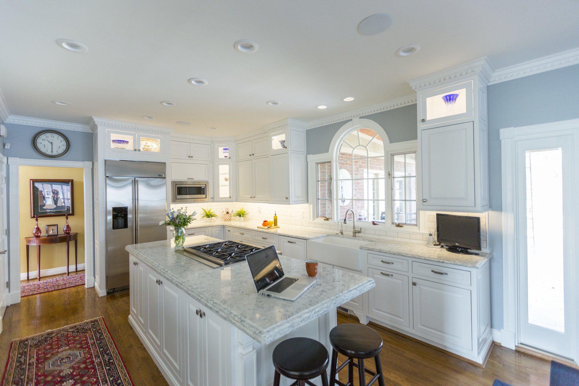 A kitchen with white cabinets and stainless steel appliances and a laptop on the counter.
