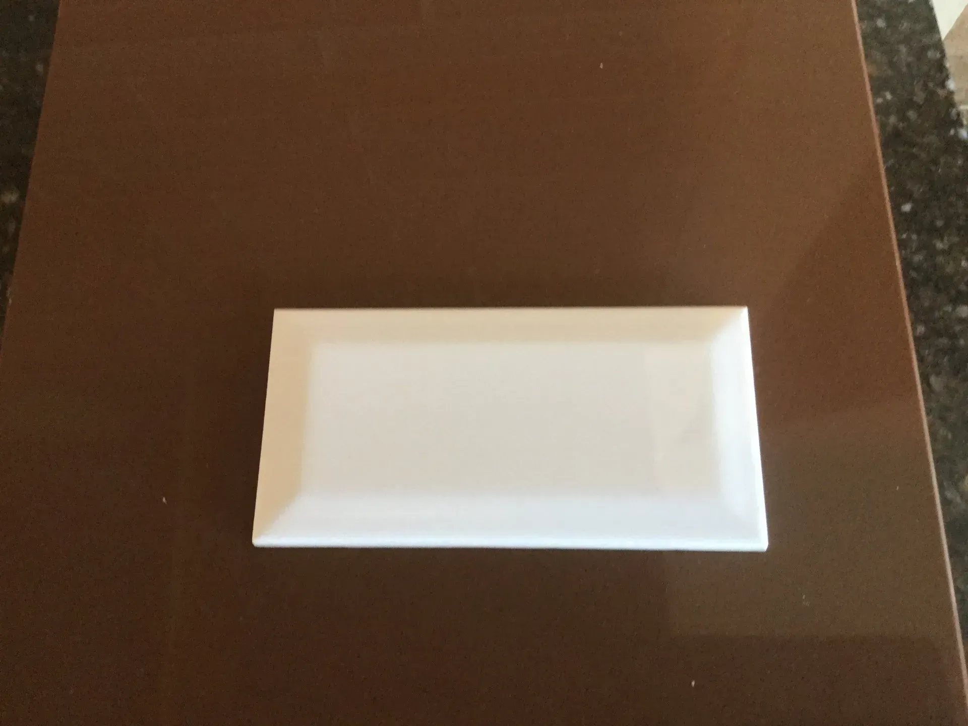 A white tile is sitting on a brown surface