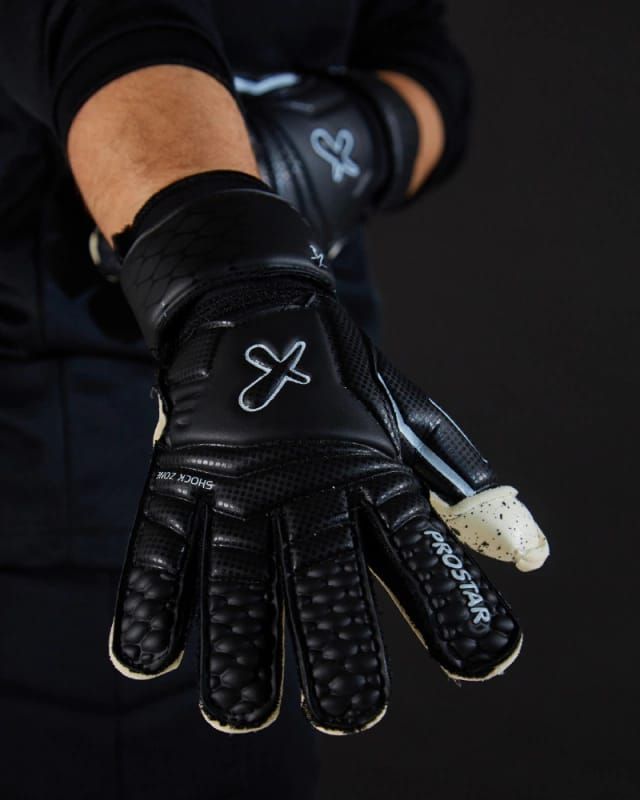 Guantes de portero, de color crema con motas y puños negros, sobre un fondo oscuro.