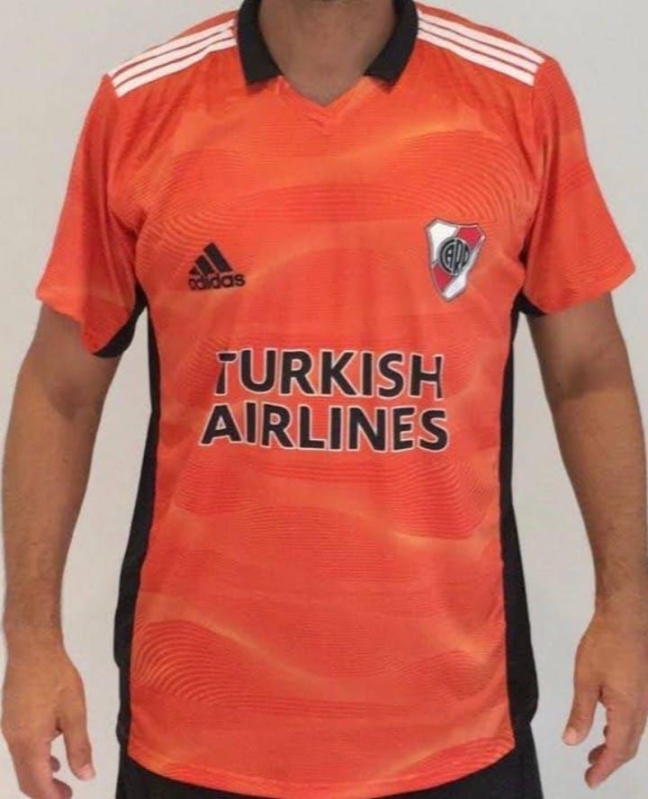 Hombre vistiendo una camiseta de fútbol de River Plate, naranja con detalles negros y el logo de Turkish Airlines.