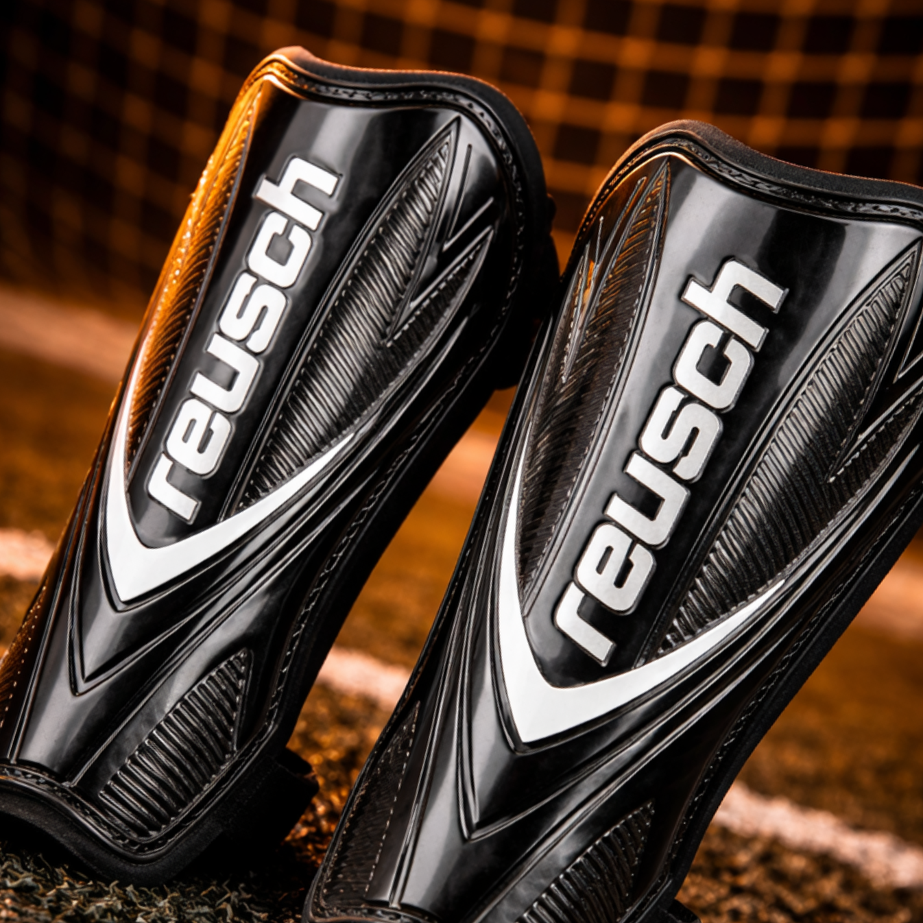 Par de espinilleras Reusch negras en un campo de fútbol.