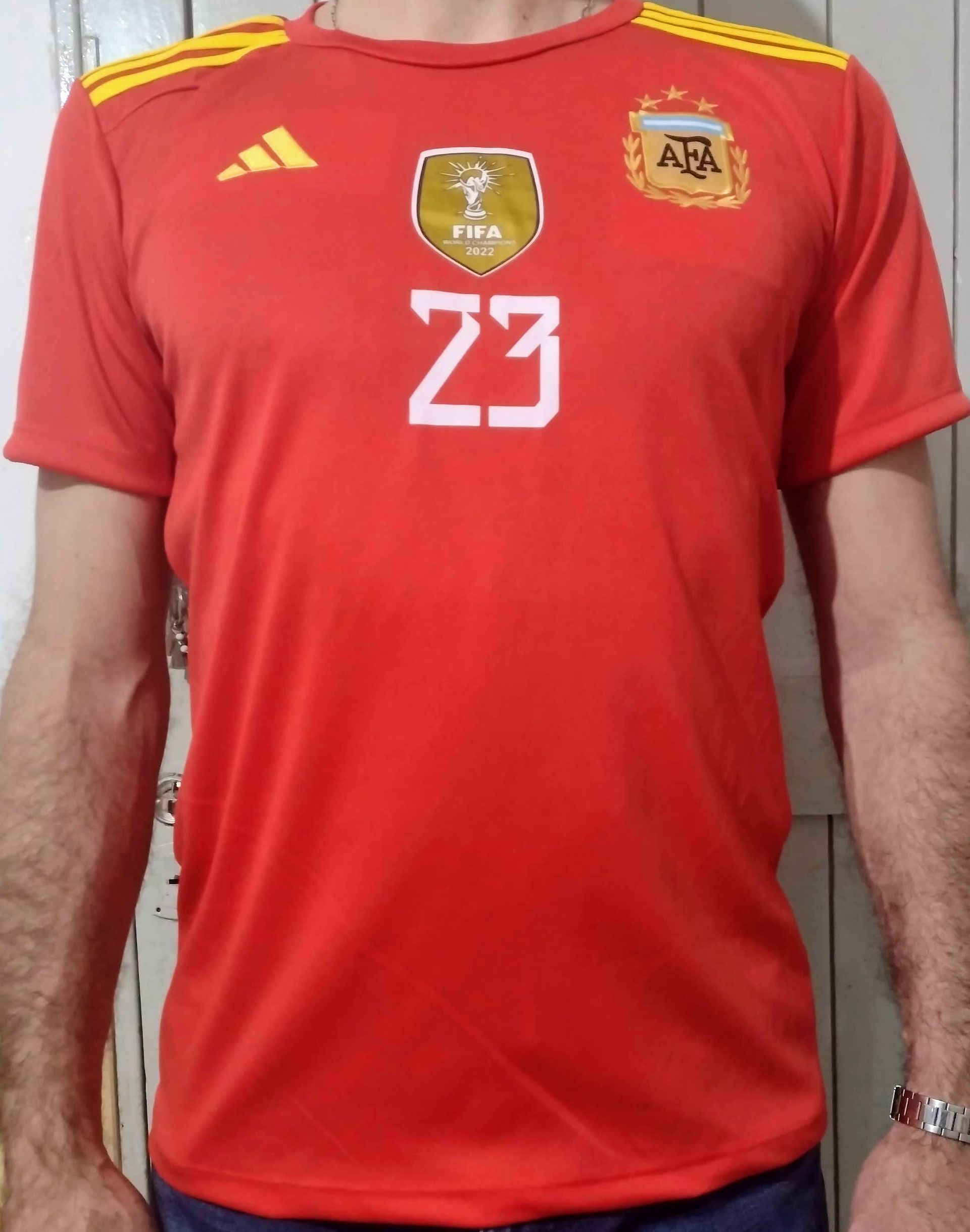 Persona que viste una camiseta de fútbol roja con el número 23, el escudo de la FIFA y el emblema de la selección argentina.