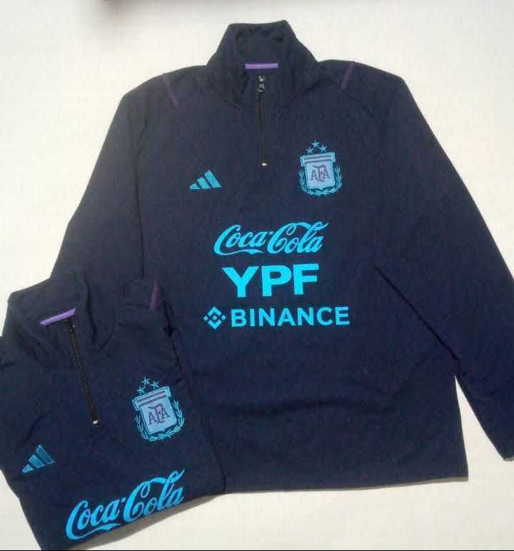 Dos chaquetas de entrenamiento de fútbol de Argentina azul marino. Una doblada y la otra extendida. Logotipos turquesa en ambas.