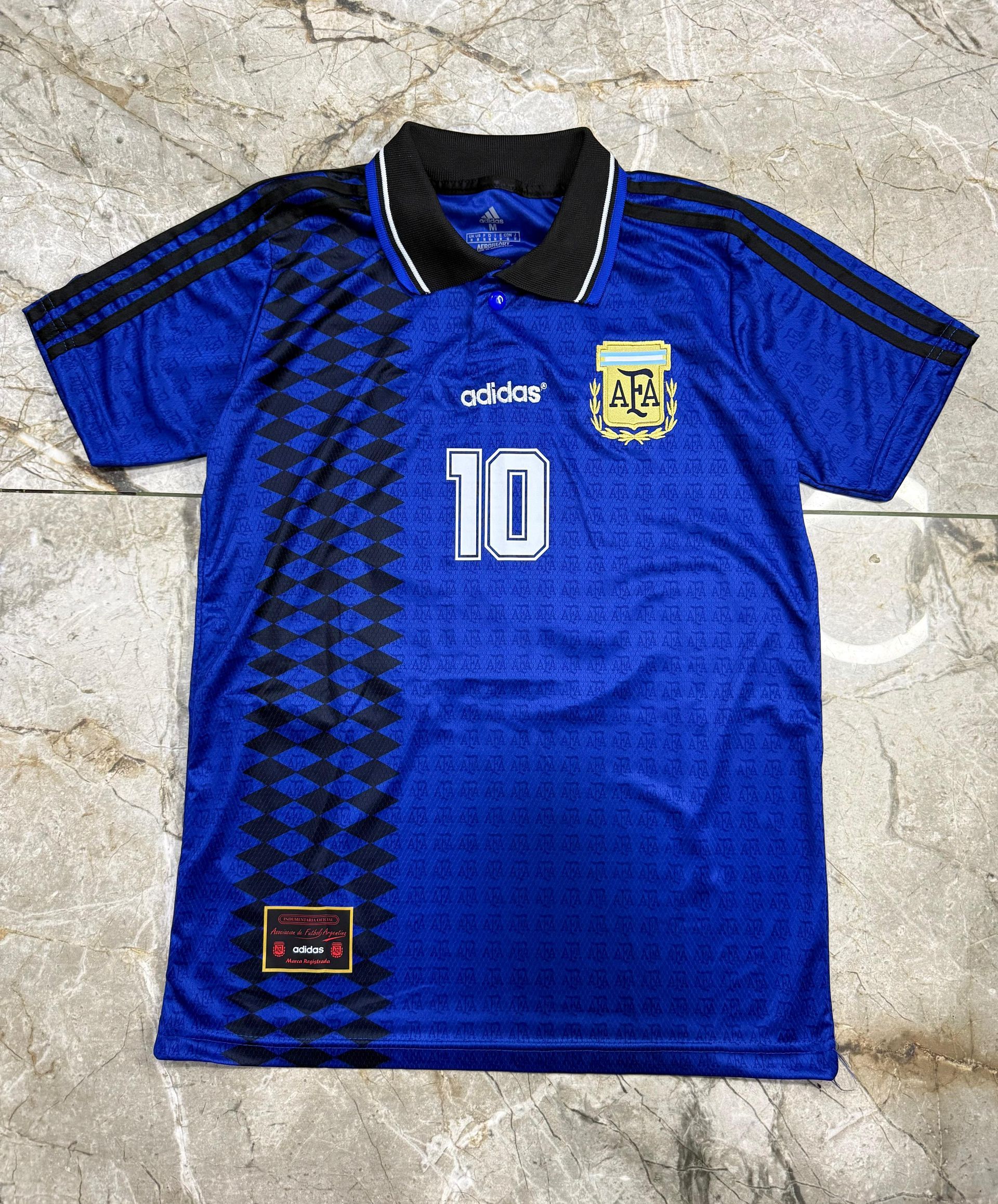 Una camiseta azul de fútbol de Adidas Argentina con cuello negro, estampado lateral negro y el número 10 impreso en la parte delantera.