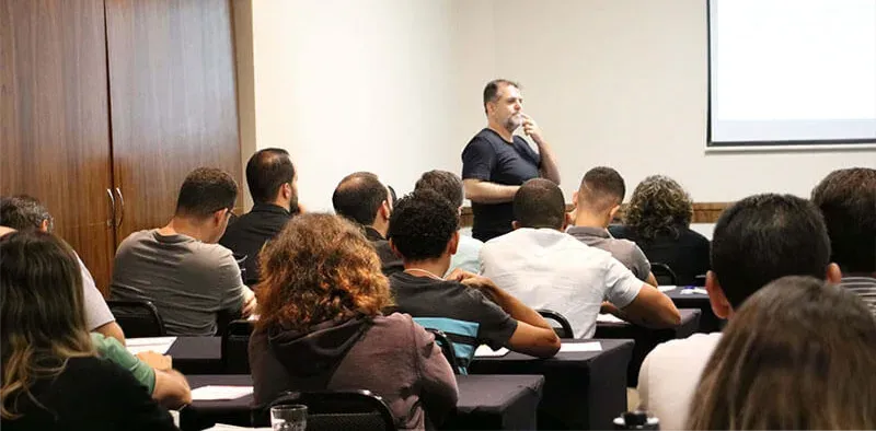 Um homem está fazendo uma apresentação para um grupo de pessoas em uma sala de aula.