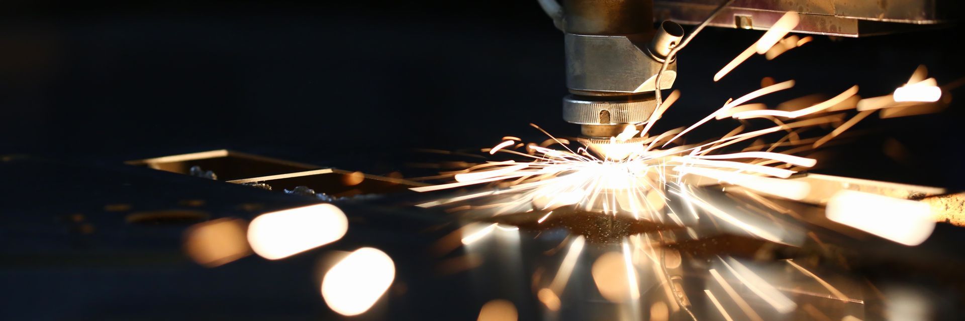 Sparks fly from a metal cutting machine, illuminating the dark workshop with bright streaks. — Bryants Laser Works in Ipswich, QLD
