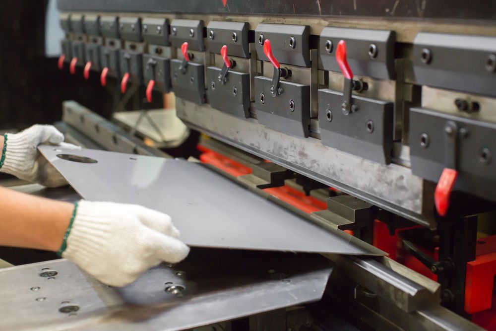 Hands Wearing White Gloves Bending Metal Sheet With an Industrial Press — Bryants Laser Works in Ipswich, QLD